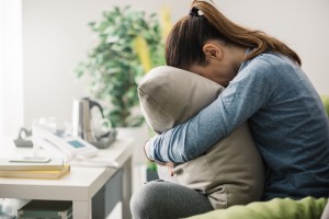 Unhappy lonely depressed woman at home she is sitting on the couch and hiding her face on a pillow depression concept