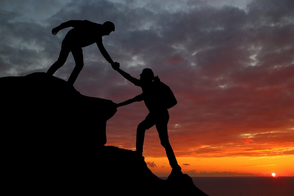 Silhouette of a man helping a woman up onto a peak