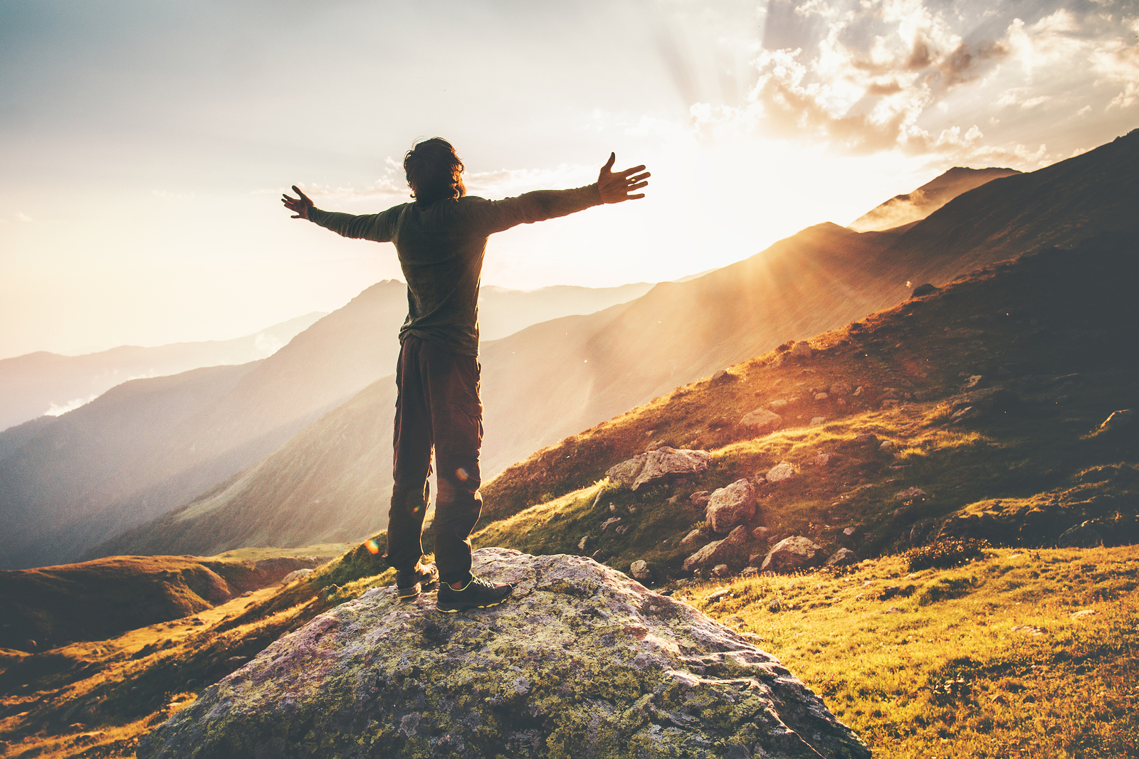 Man standing on a with arms spread wide looking up a the sunlight breaking through the clouds