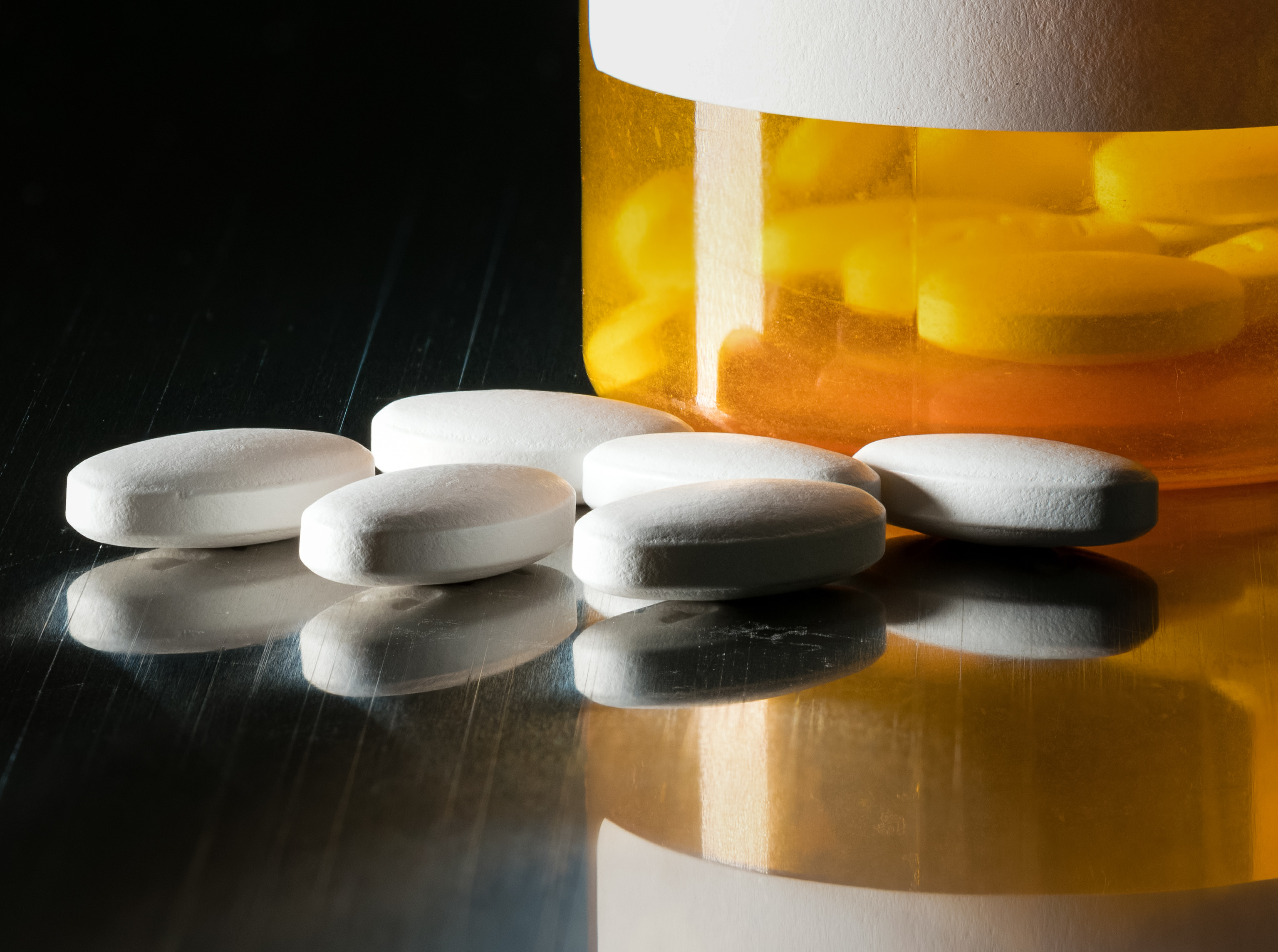 Prescription bottle with blank label for copy space and white pills or tablets on metal table for opioid epidemic illustration