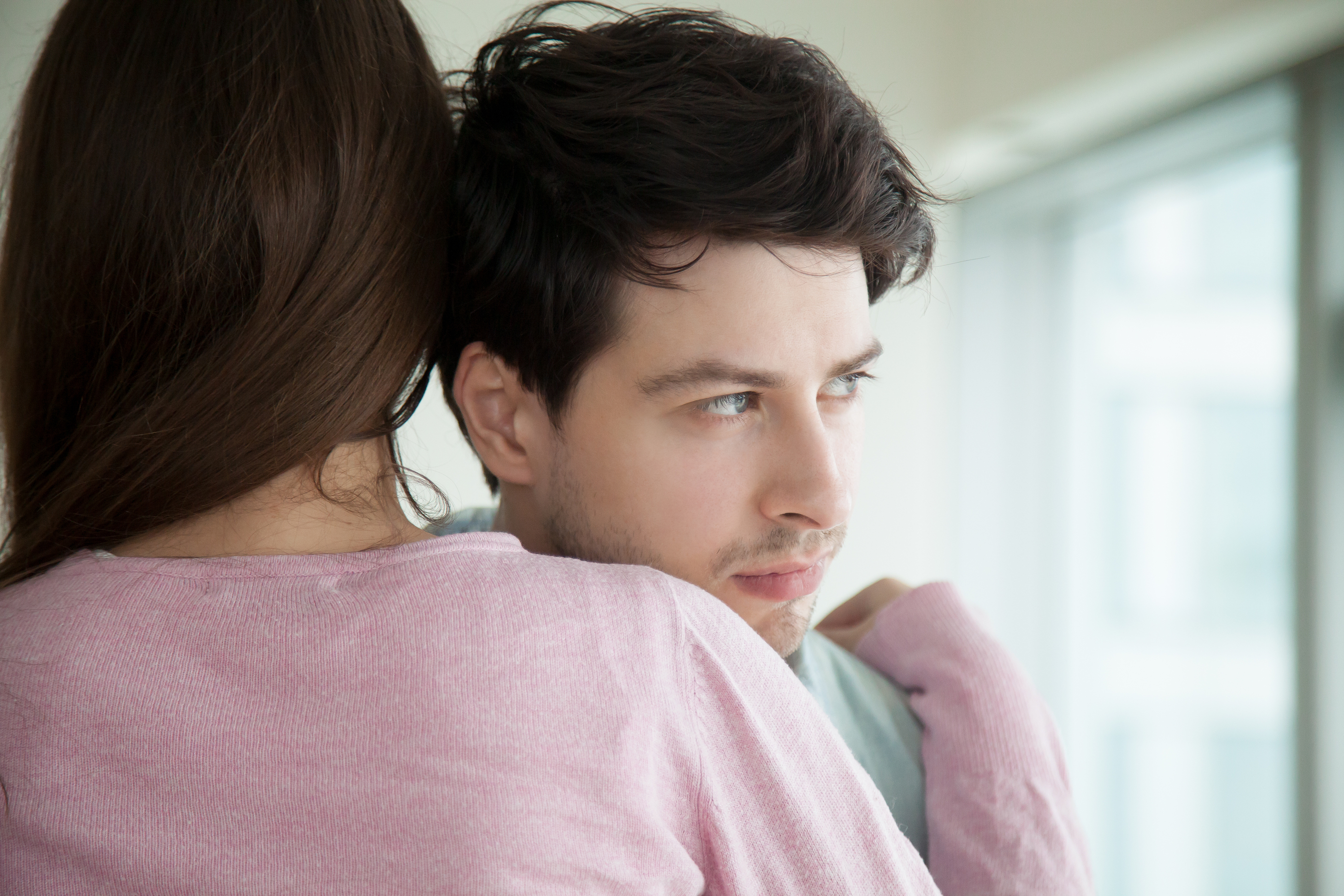 Supportive_Hug_JPG Woman hugging her upset boyfriend, sad guy looking away through the window, loving wife supporting husband, embracing and comforting him, helping to solve business problems, couple reconciliation