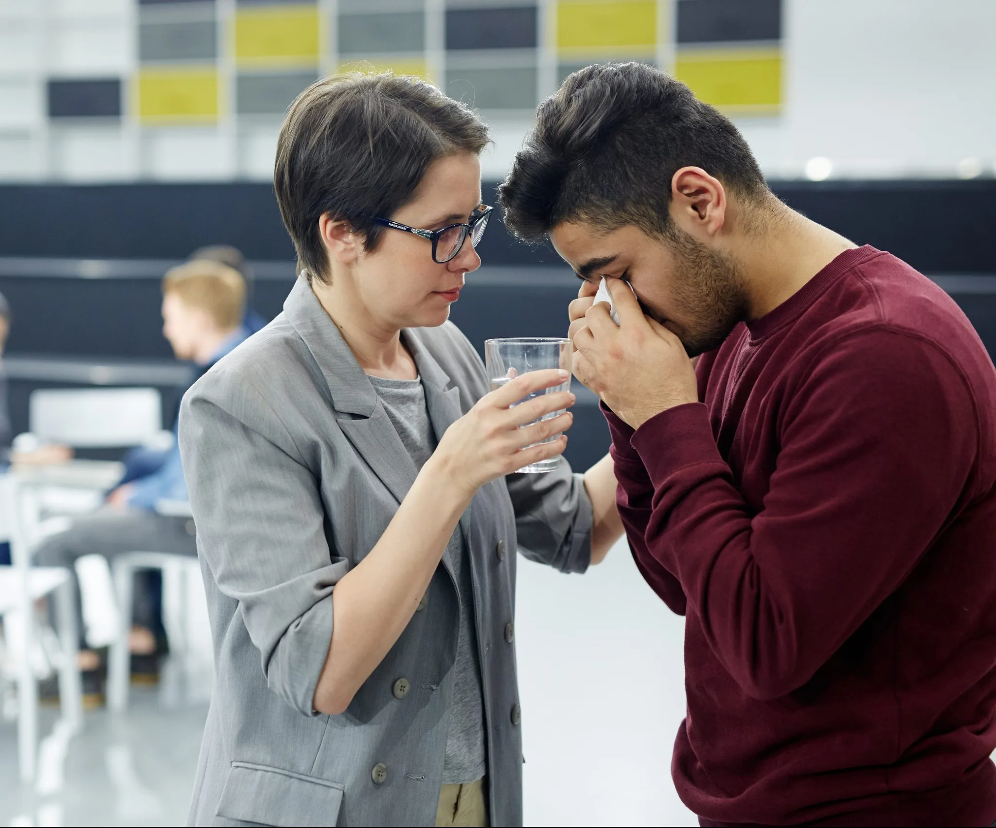 Helpful woman with glass of water comforting crying groupmate or patient
