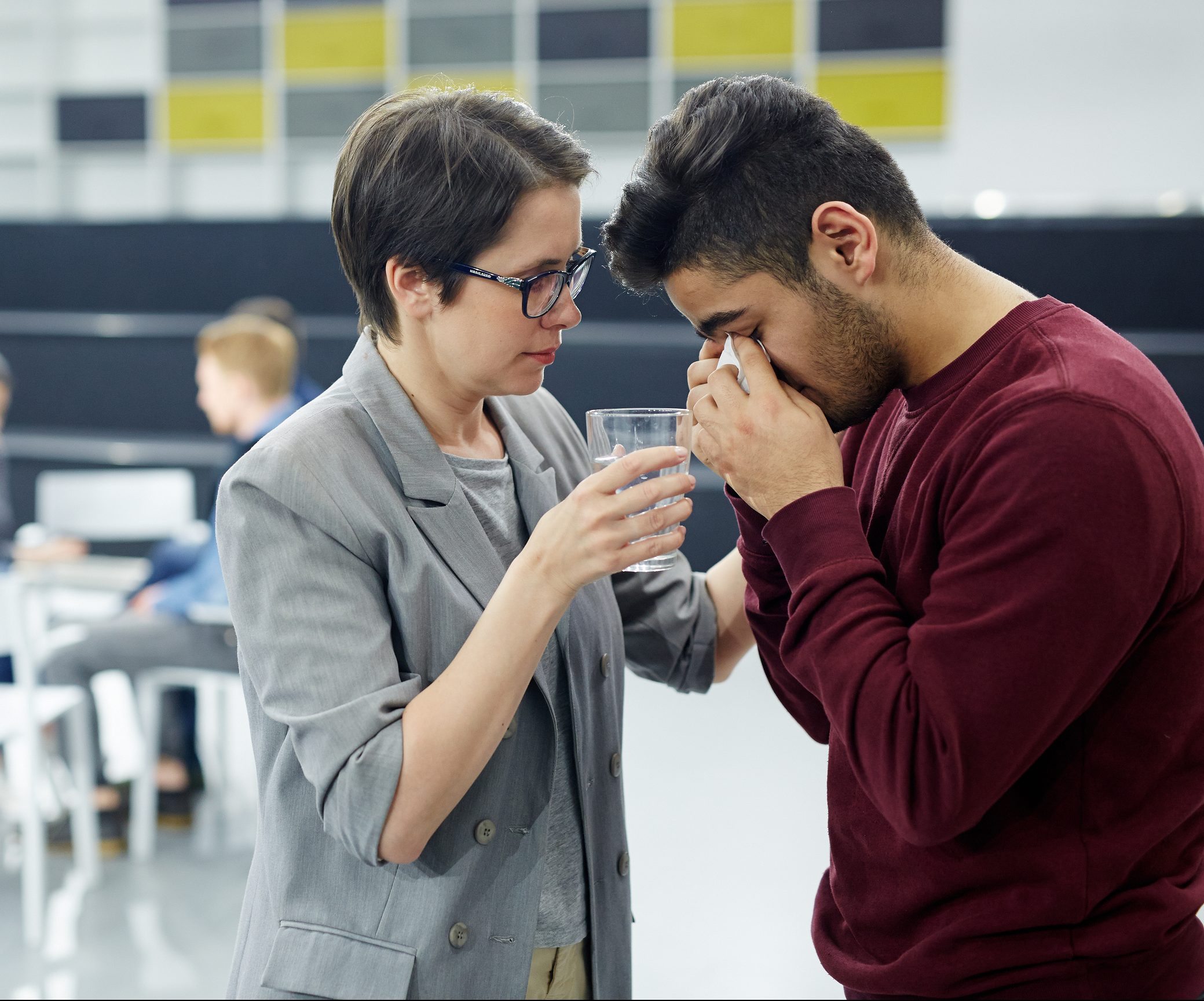 Helpful woman with glass of water comforting crying groupmate or patient