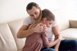 bigstock–185095969 (1) Young tender husband hugging his wife, loving man embracing woman gently and tightly sitting on couch at home, showing love and support, happy soulmates or close friends, peace, harmony, understanding