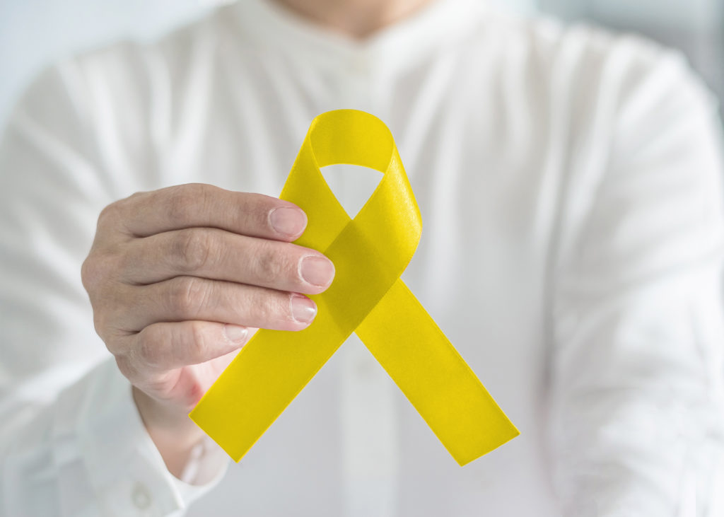 Yellow ribbon symbolic color for suicide prevention and Sarcoma Bone cancer awareness in person's hand