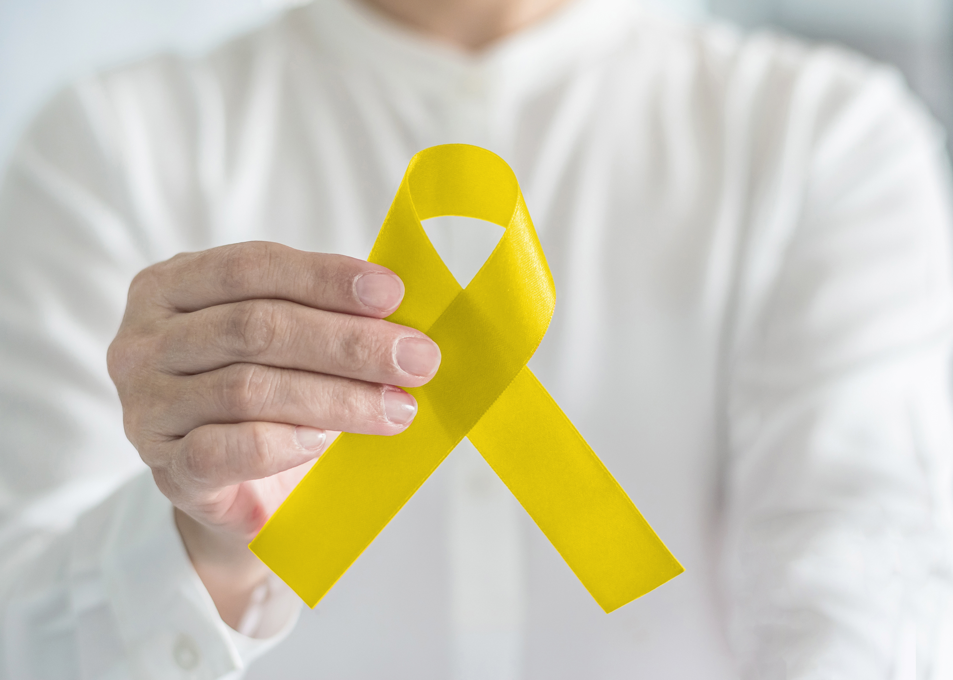 Yellow ribbon symbolic color for suicide prevention and Sarcoma Bone cancer awareness in person's hand