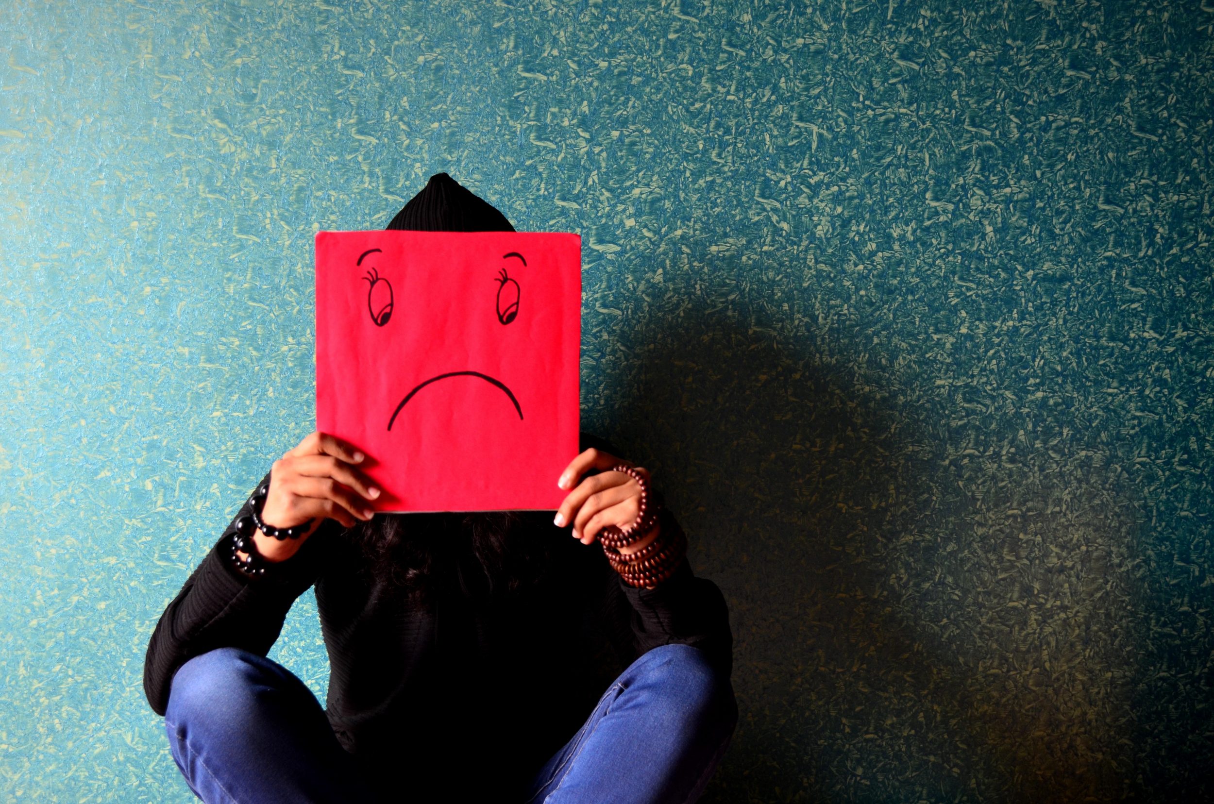 pexels-photo-278312 Person holding up a square colored piece of paper with a sad face on it