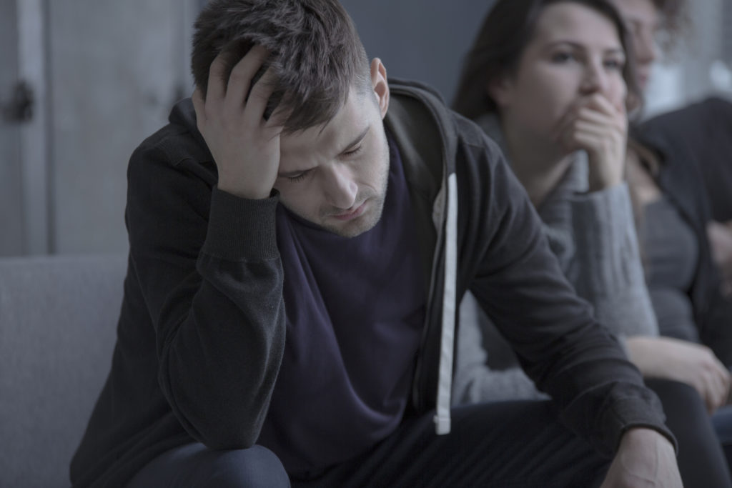 Depressed man with alcoholism problem sitting in dark rehab center