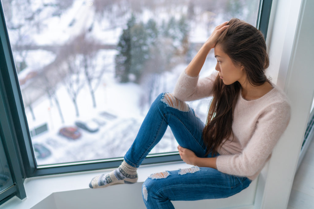 Winter depressed sad girl lonely by home window looking at cold