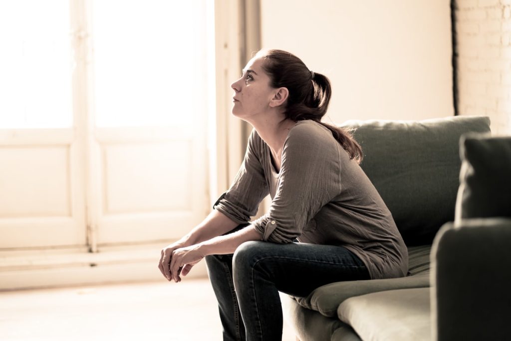 A young woman sits on a couch in her apartment as she suffers from health anxiety