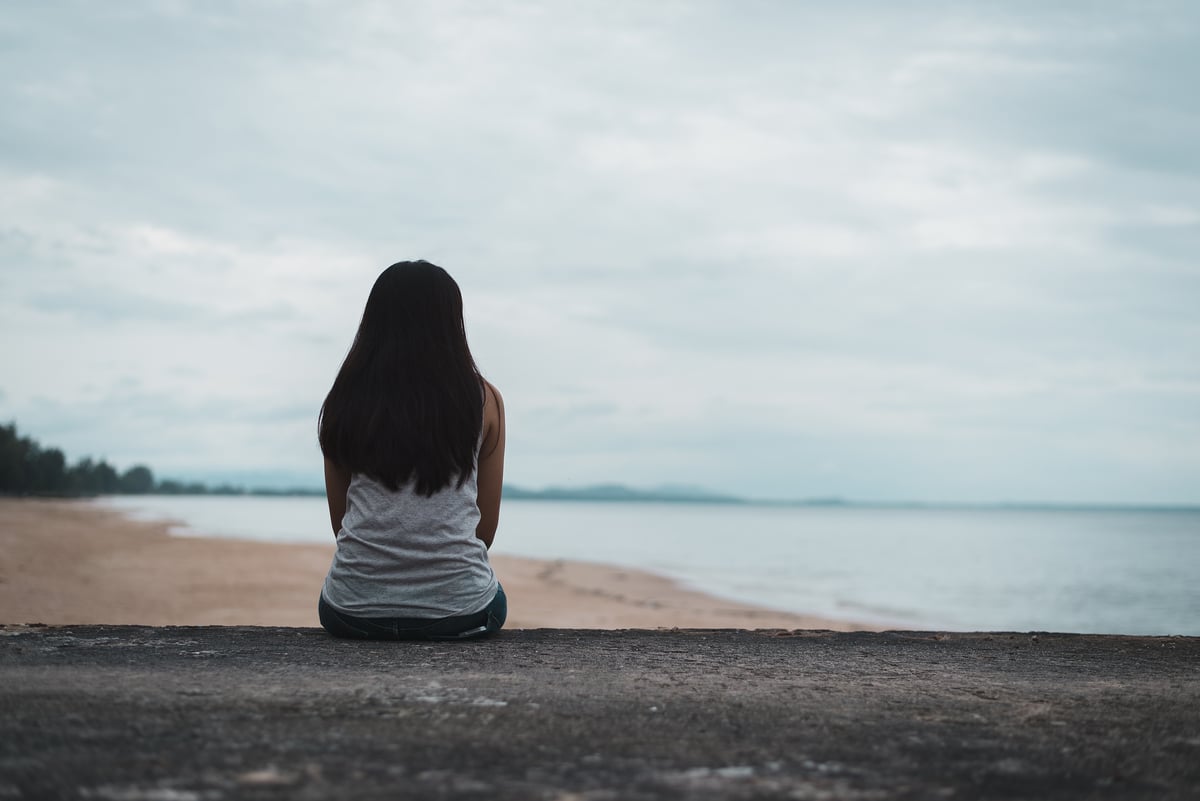 A young woman who suffers from bipolar disorder sits outside, looking toward the shoreline of the beach during a depressive episode.