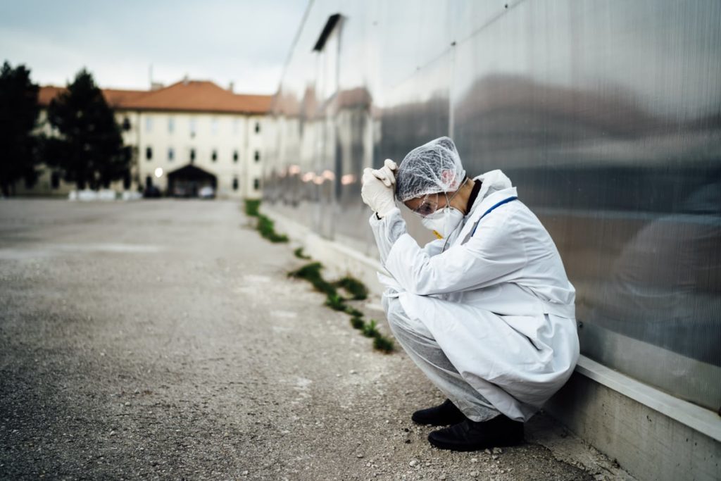 A doctor crouches down against the wall of a medical facility, overwhelmed with emotion.