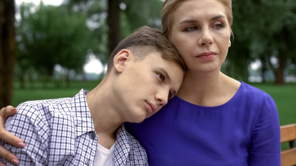 A mother comforts her teenage son during the COVID-19 pandemic