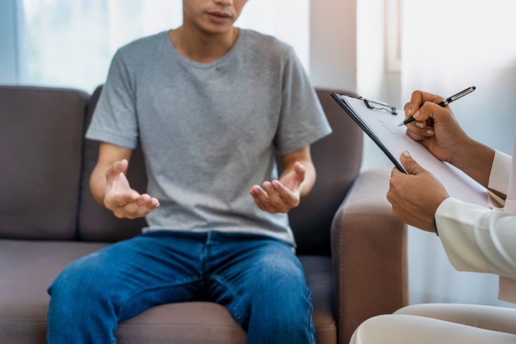 A young man sits across from a therapist. They review his experiences with disordered eating and mental health disorders.