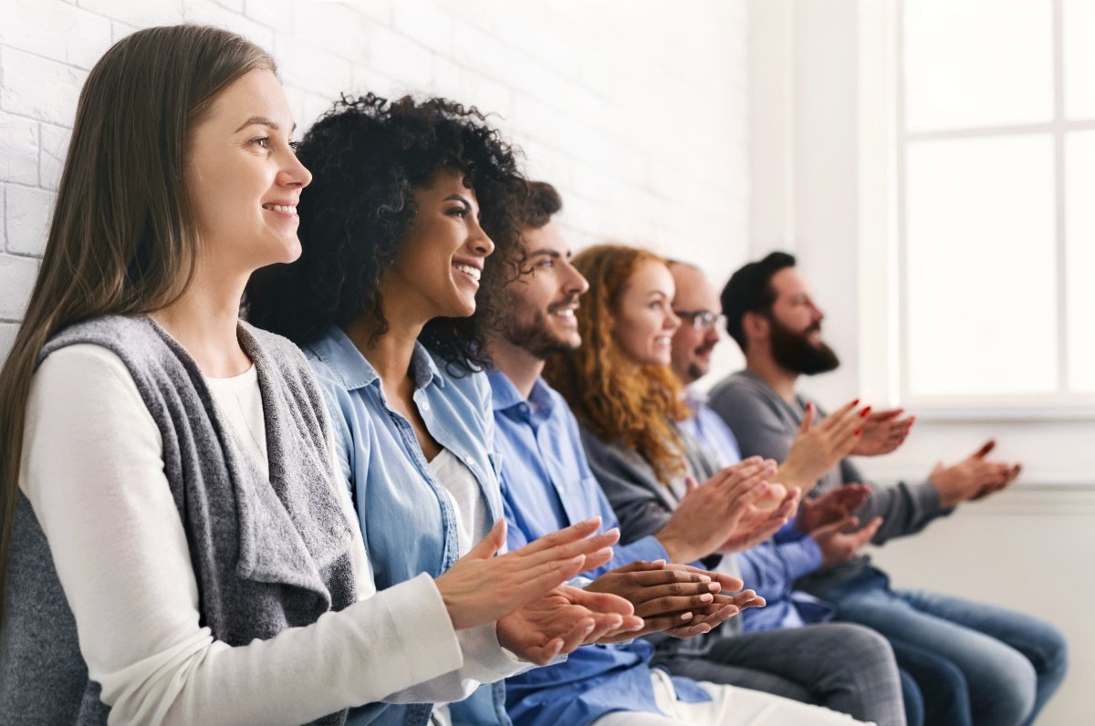 A group of people sit in a row and applaud an individual who has shared their sobriety challenges at a 12 step program meeting