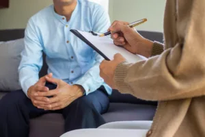 patient in treatment for depression A patient sits across from a therapist during a treatment session for depression. The therapist is holding a clipboard and taking notes, while the patient sits across from the therapist, explaining their symptoms.