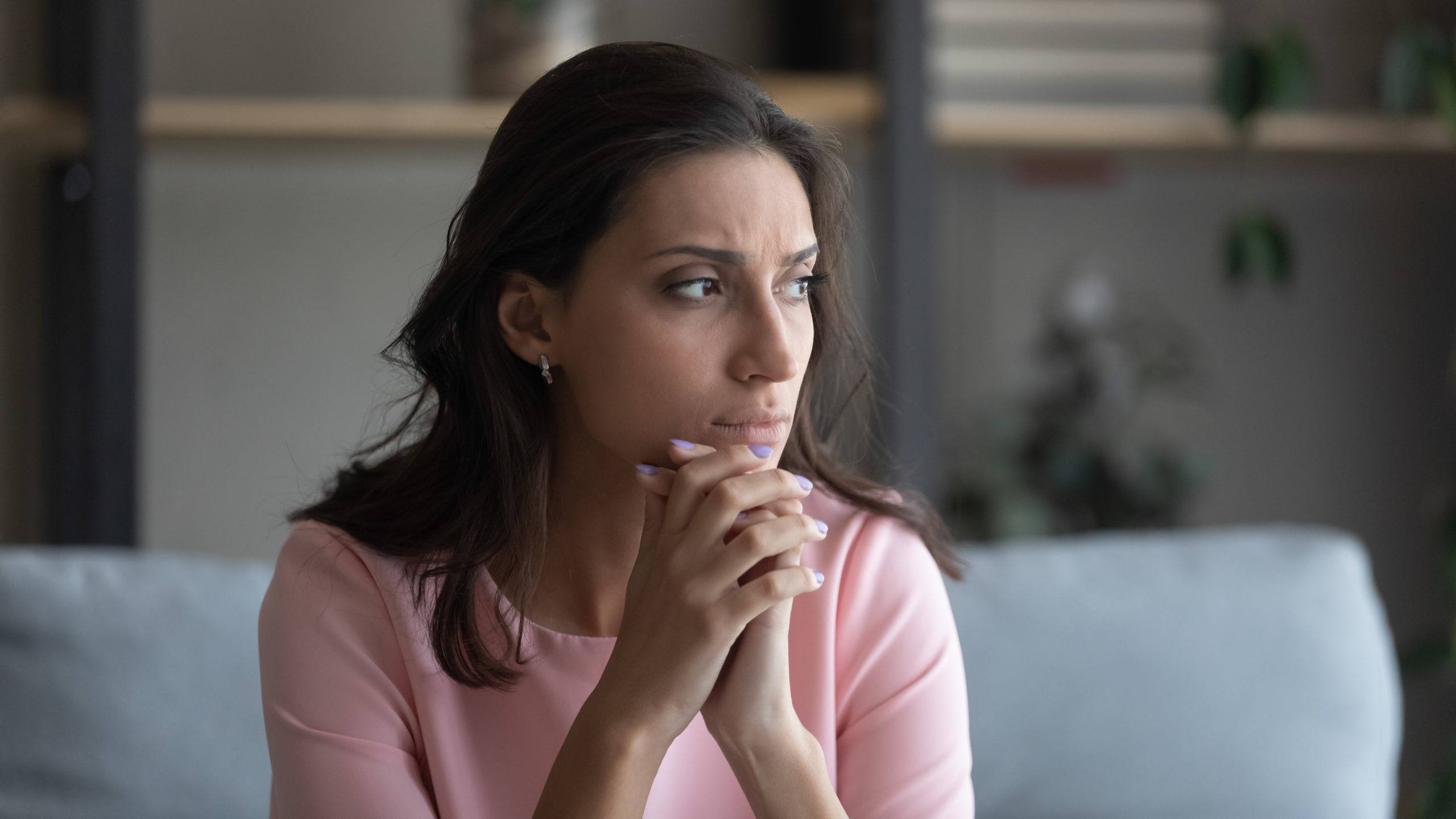 Worried young indian Arabic woman sit on couch at home look in distance thinking pondering, anxious unhappy arab mixed race female suffer from mental psychological personal problems, mourn or yearn