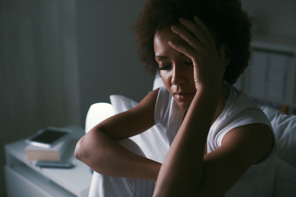 Sad depressed woman suffering from insomnia, she is sitting in bed and touching her forehead, sleep disorder and stress concept