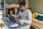 African-American man sitting at the table in the living room and search information about medicine on the internet