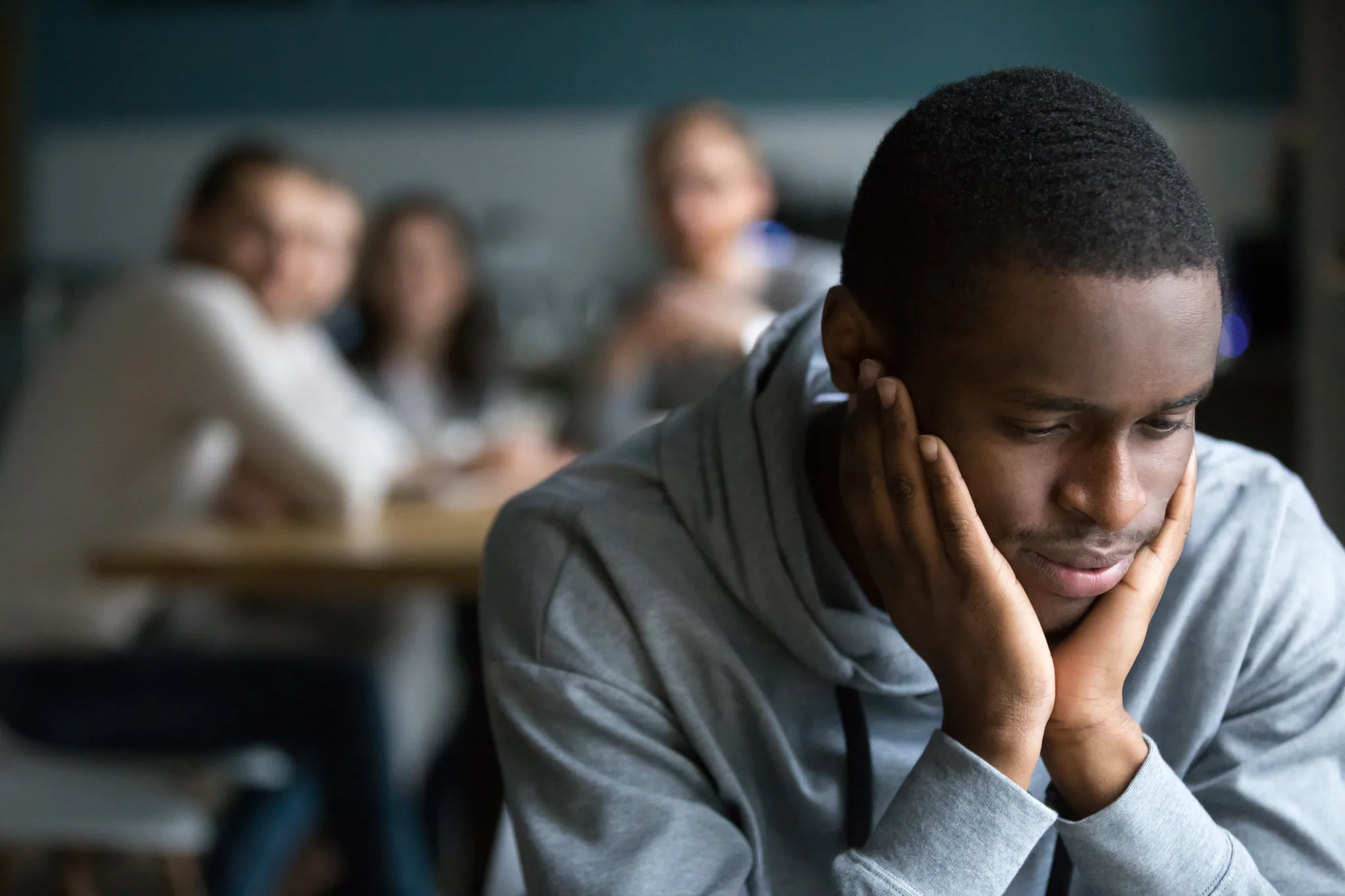 African American millennial guy feel lonely sitting alone in cafÃ©, offended black student avoid talking to friends having misunderstanding, young man outcast suffer from racial discrimination