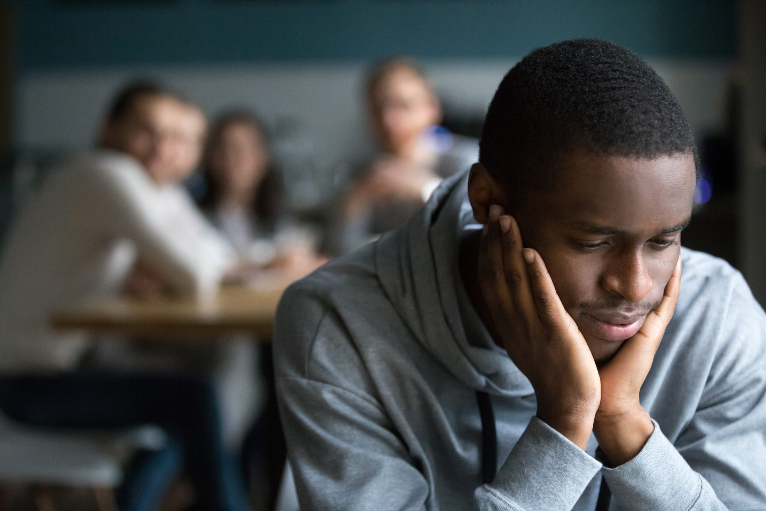 African American millennial guy feel lonely sitting alone in cafÃ©, offended black student avoid talking to friends having misunderstanding, young man outcast suffer from racial discrimination