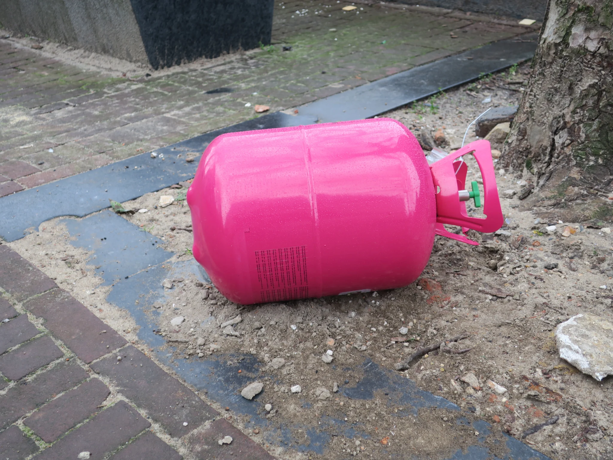 empty pink colored nitrous oxide tank laying on the stree