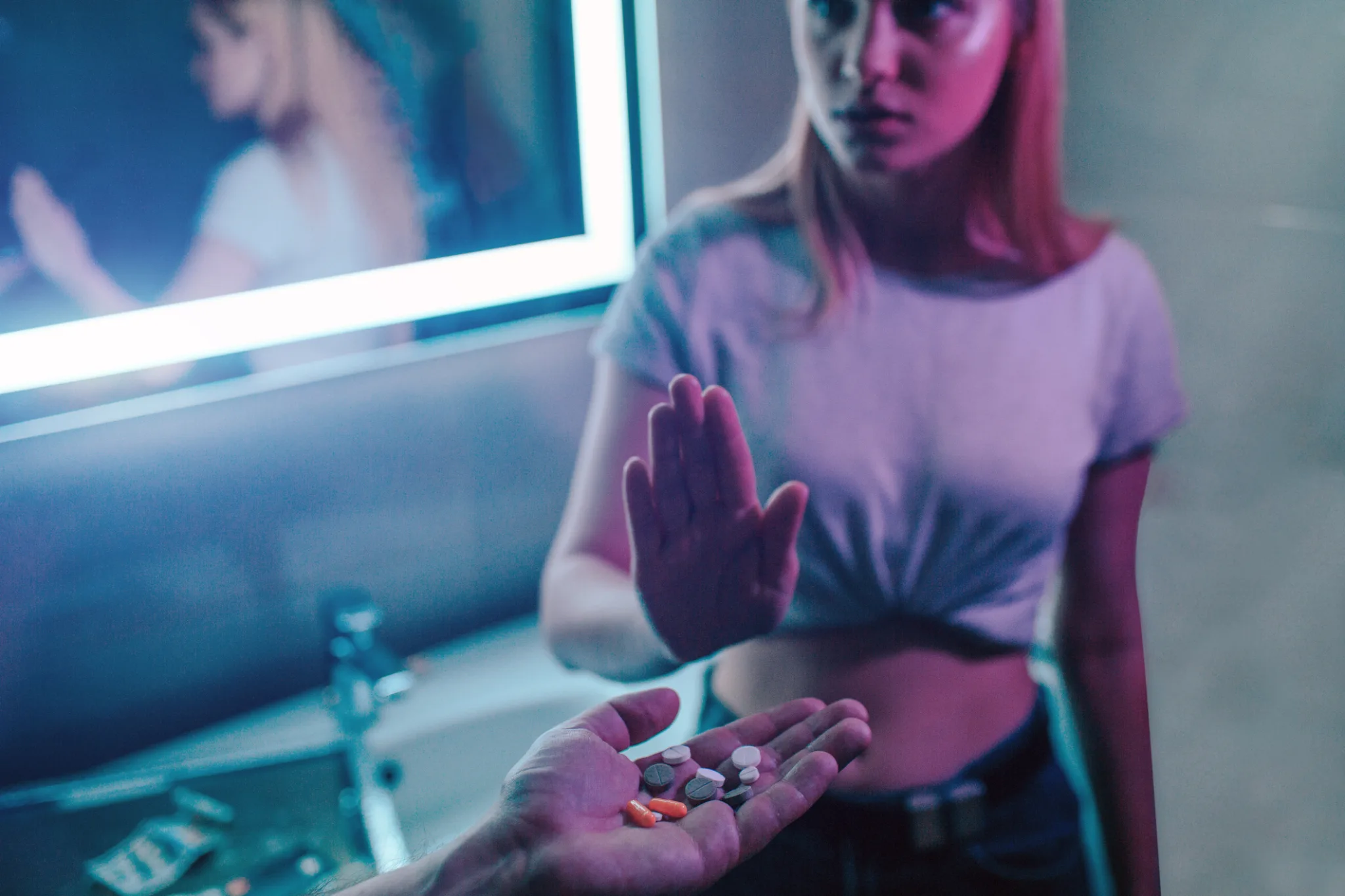 No drugs. Refusal skills. Reject drugs offer. Hand saying NO. Young woman shows an open palm against drugs offer while hand holding colorful drugs in night club.