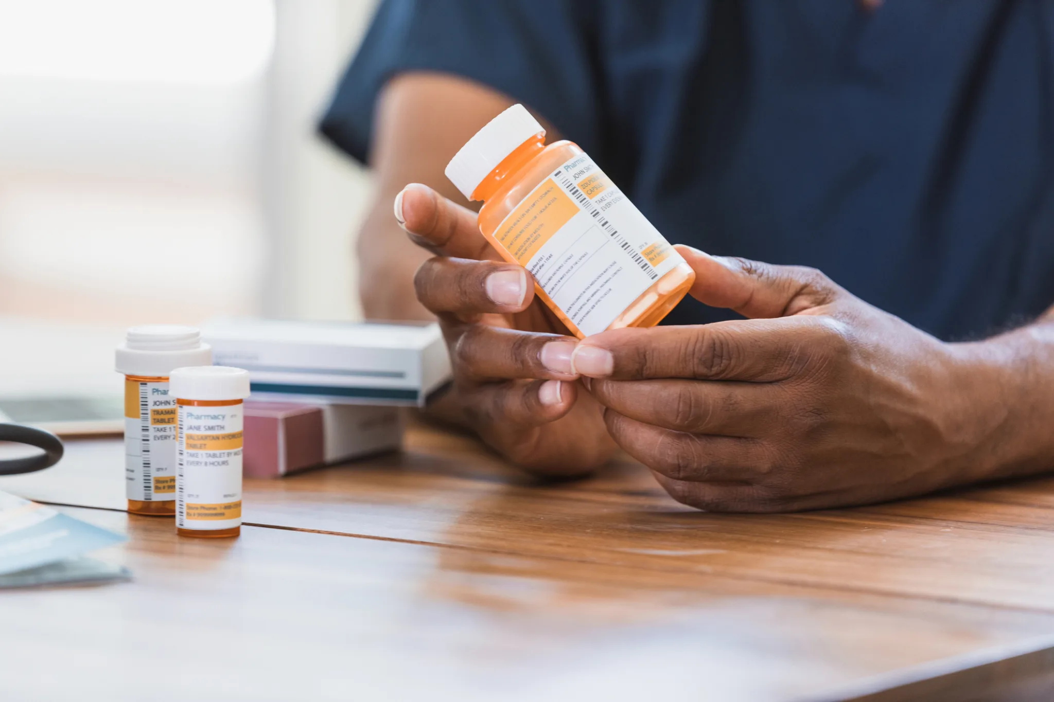 Nurse holding bottle of pills with other bottles resting on table next to her hand as she explains medication half life to a patient