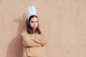 Unhappy woman wearing bunny ears headband struggling with her mental health while celebrating Easter