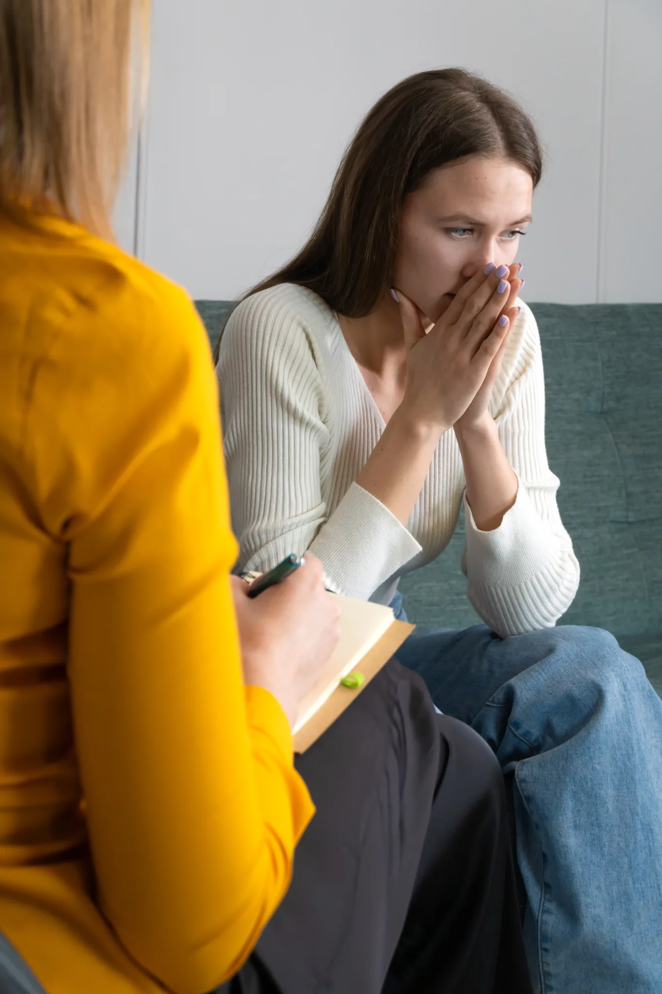 Young sad woman is sitting on the couch, holding her hands to her face at a psychotherapist's appointment working on biofeedback