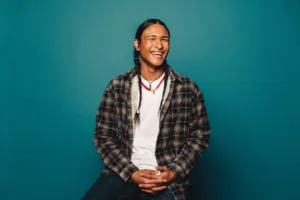 Young native american man sitting in front of blue background