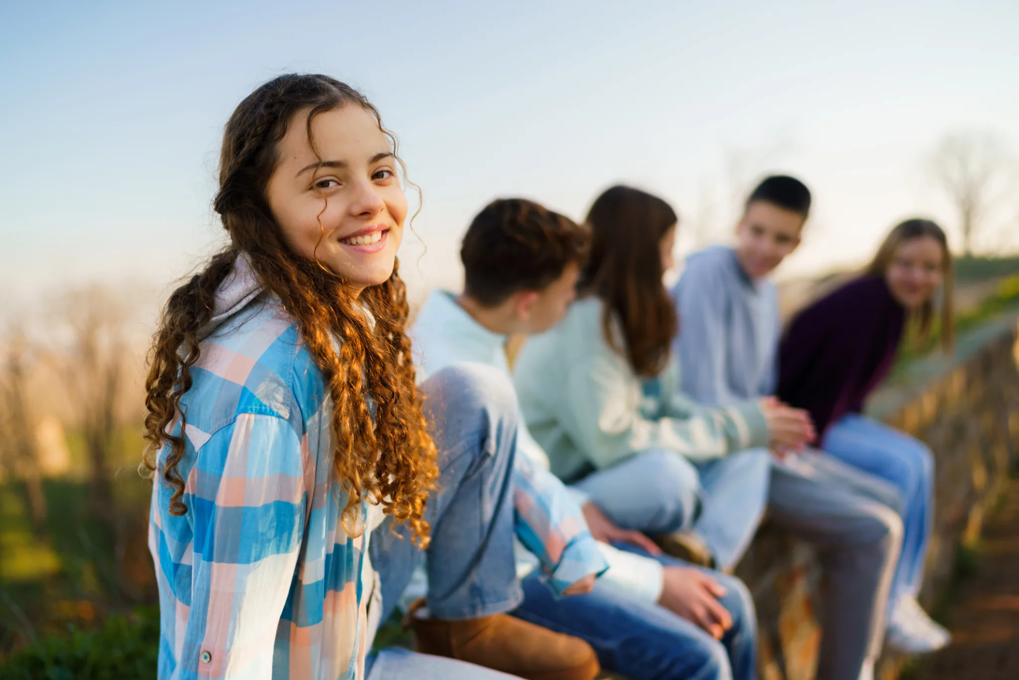 Happy teenage girl sitting on a wall whit her friends outdoors