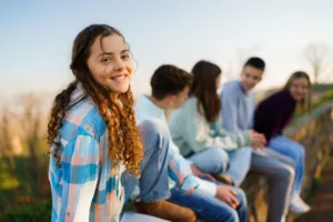 Happy teenage girl sitting on a wall whit her friends outdoors