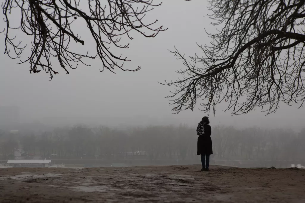 Girl standing alone in the park on gloomy day.