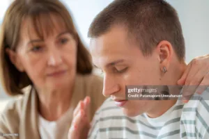 In a serious living room conversation, a teenage son argues while his concerned mother offers encouragement. This emotional family scene highlights communication challenges, love, support, and the parenting struggles of adolescence and understanding.