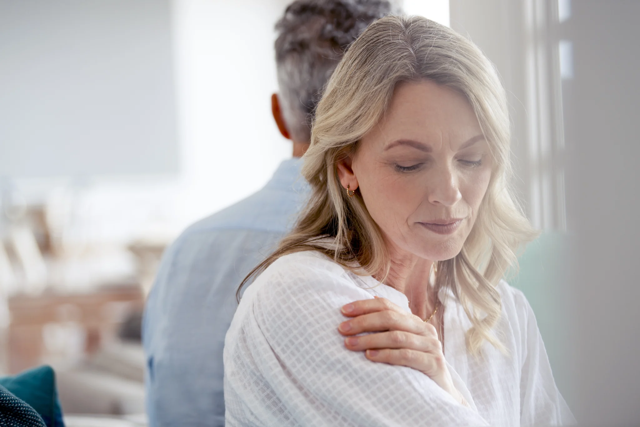 Mature couple fighting at home sitting on the sofa. They are sitting back to back not talking. The woman looks sad and depressed