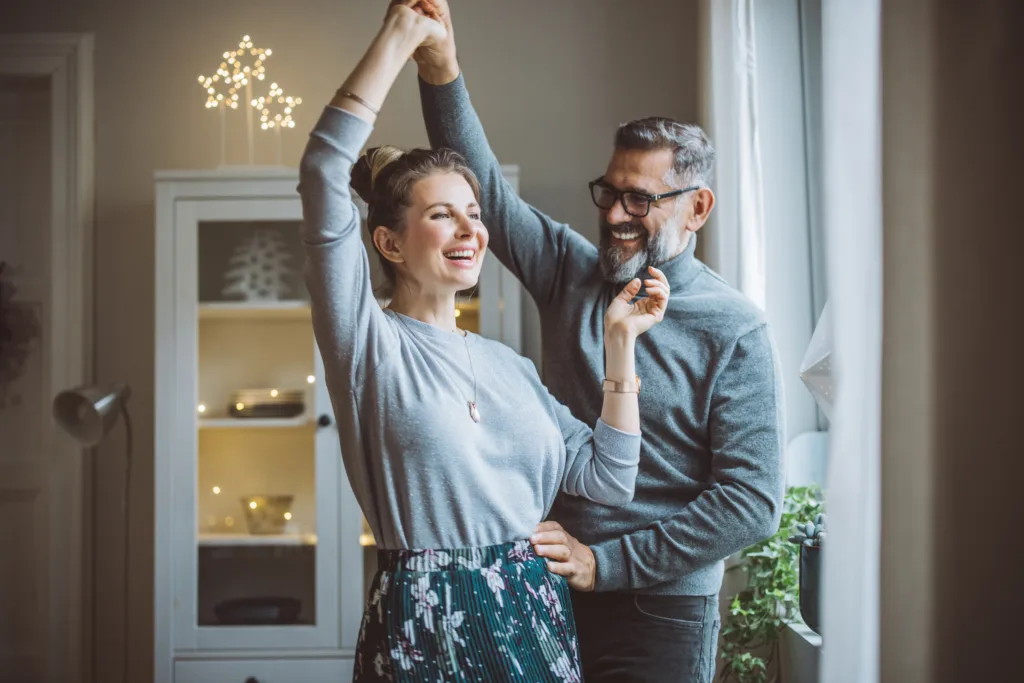 Mature couple for Christmas at home. They are standing in front of window and dancing.