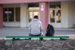 one-young-man-sitting-on-bench-at-school-yard-break-time-back-view-stockpack-gettyimages One young man sitting on bench at school yard. Break time. Back view.
