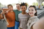 POV shot of diverse group of teens taking selfie photo outdoors in urban area and smiling at camera