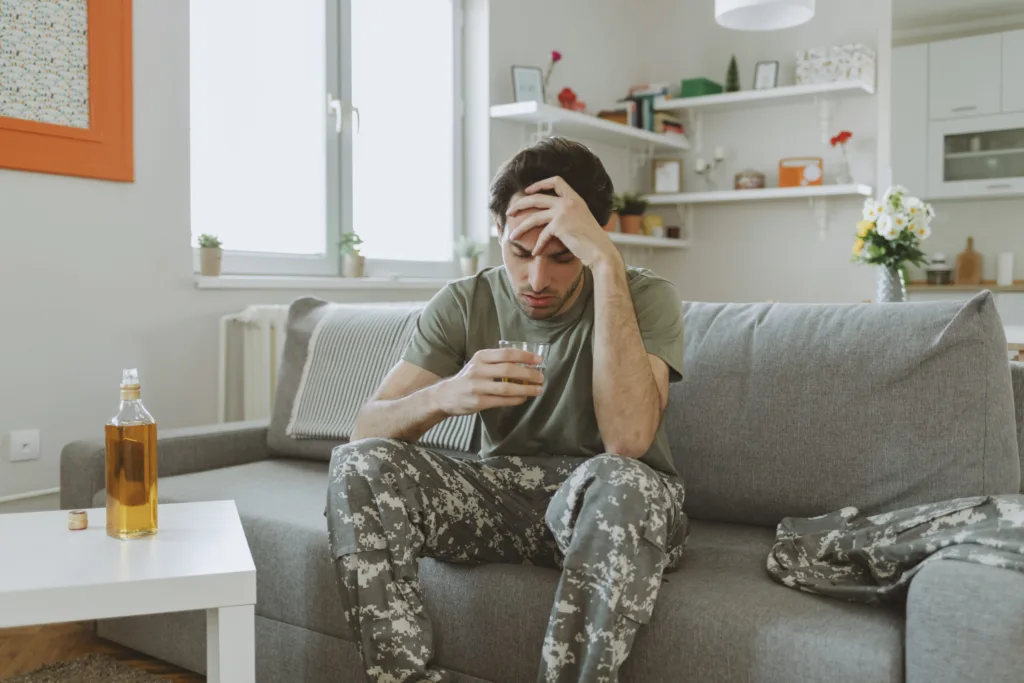 Sad Army Veteran Soldier Marine Sitting in Living Room, Drinking Whiskey at Home Alone.