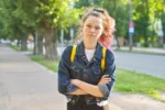 Serious teen schoolgirl with backpack, hands crossed, outdoor
