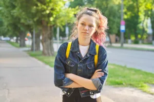 Serious teen schoolgirl with backpack, hands crossed, outdoor