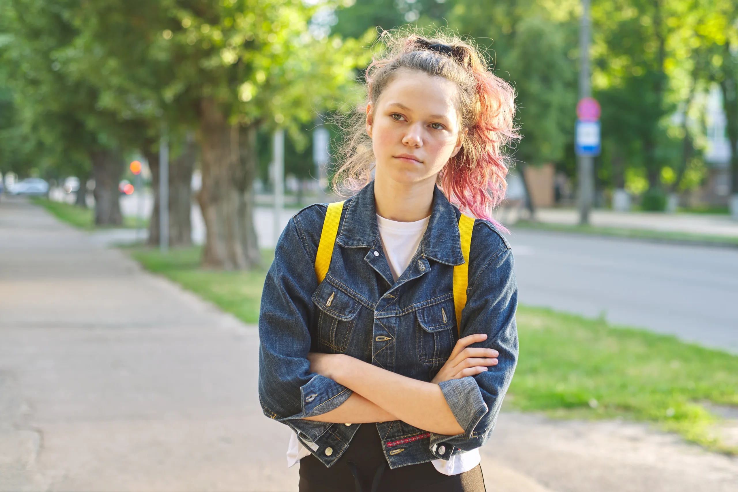 Serious teen schoolgirl with backpack, hands crossed, outdoor