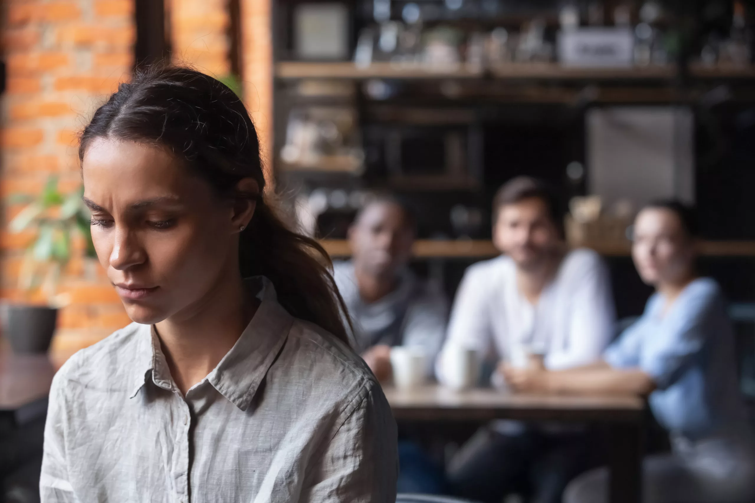 Upset mixed race woman suffering from bullying, discrimination, excluded girl having problem with bad friends, feeling offended and hurt, sitting alone in cafe, avoiding people, social outcast