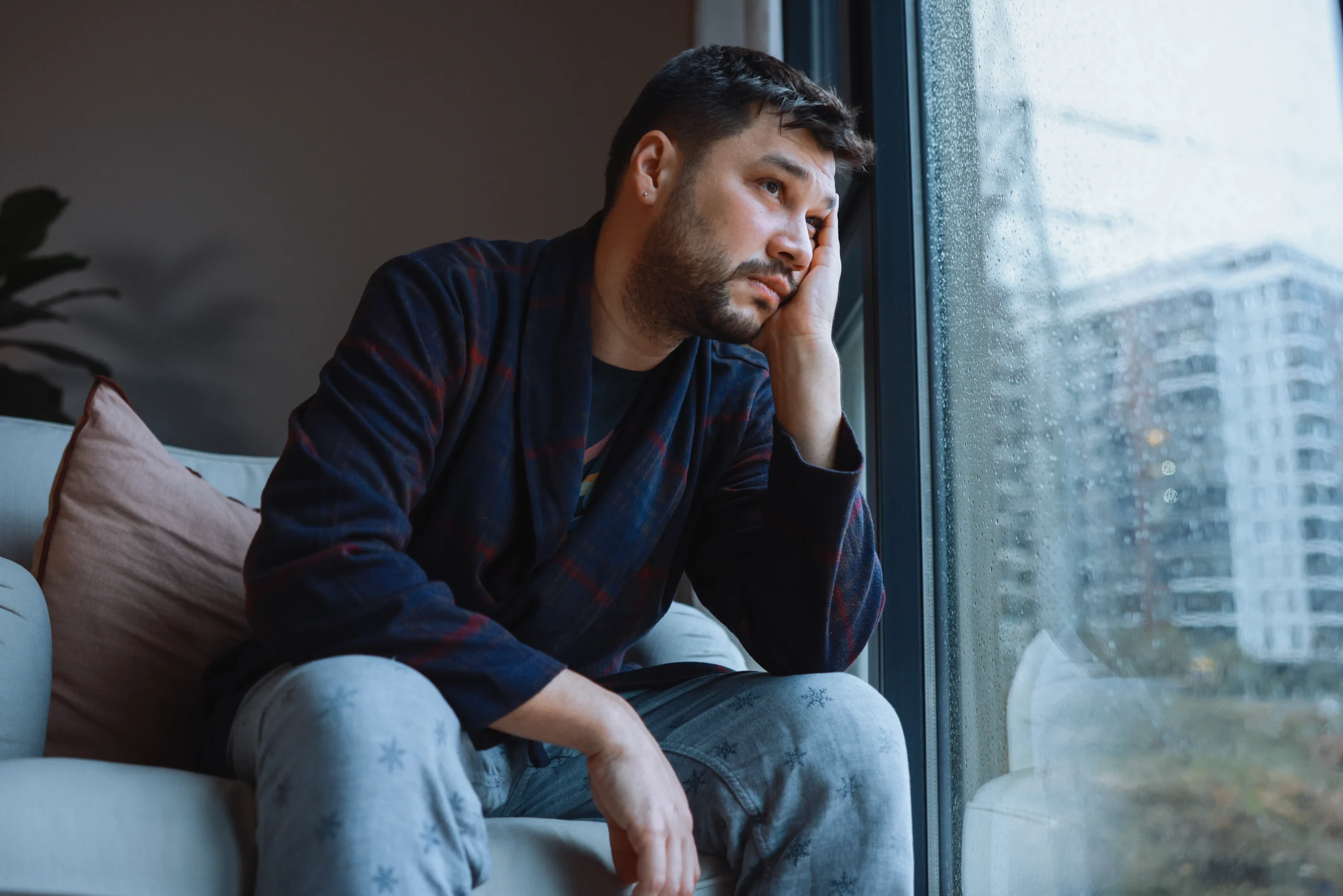Very bored and sad men leaning on the window of her house looking away for so much time of isolation