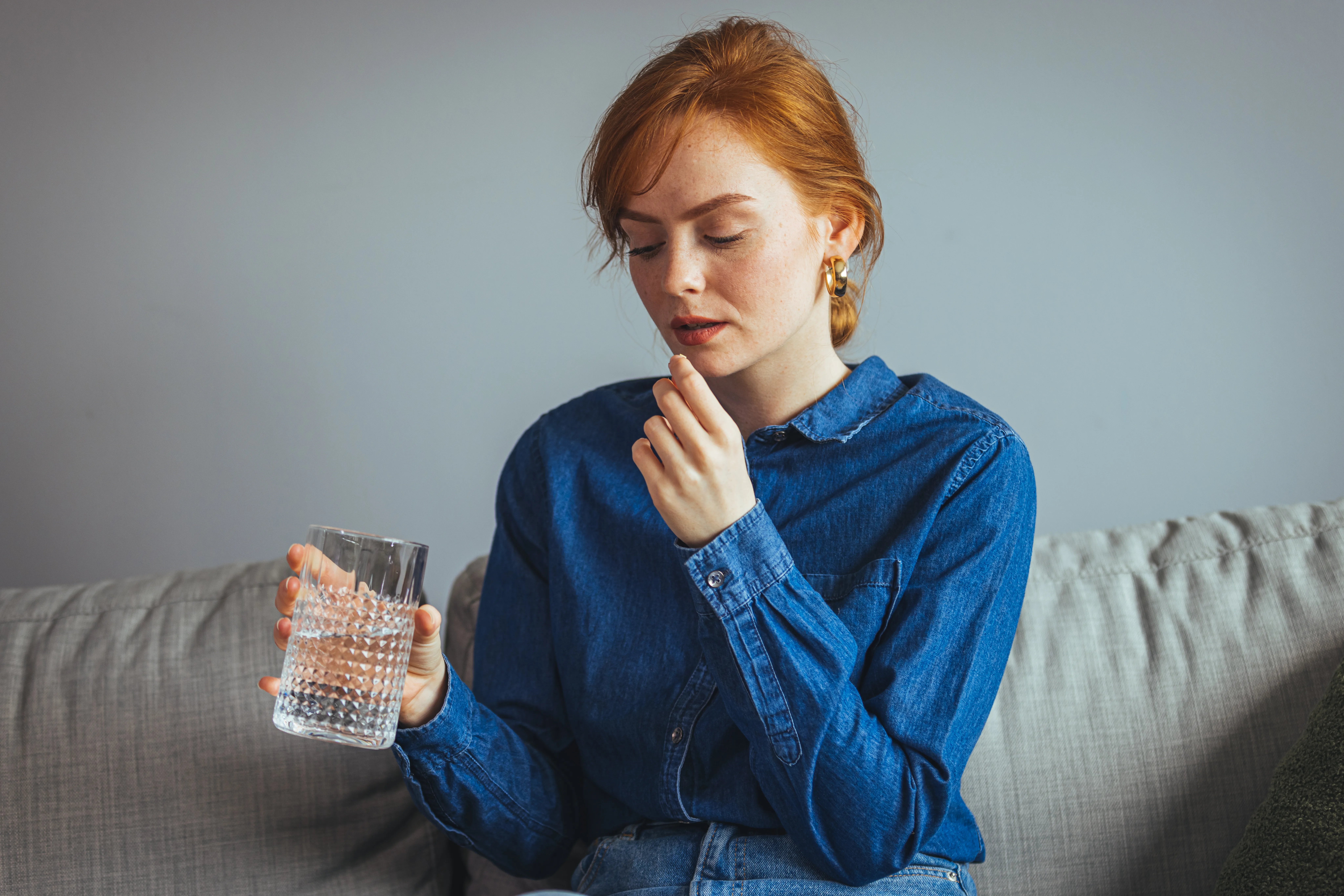 Young beautiful woman taking tablet with glass of fresh water. Close up of woman holding a glass of water and medication in her hand