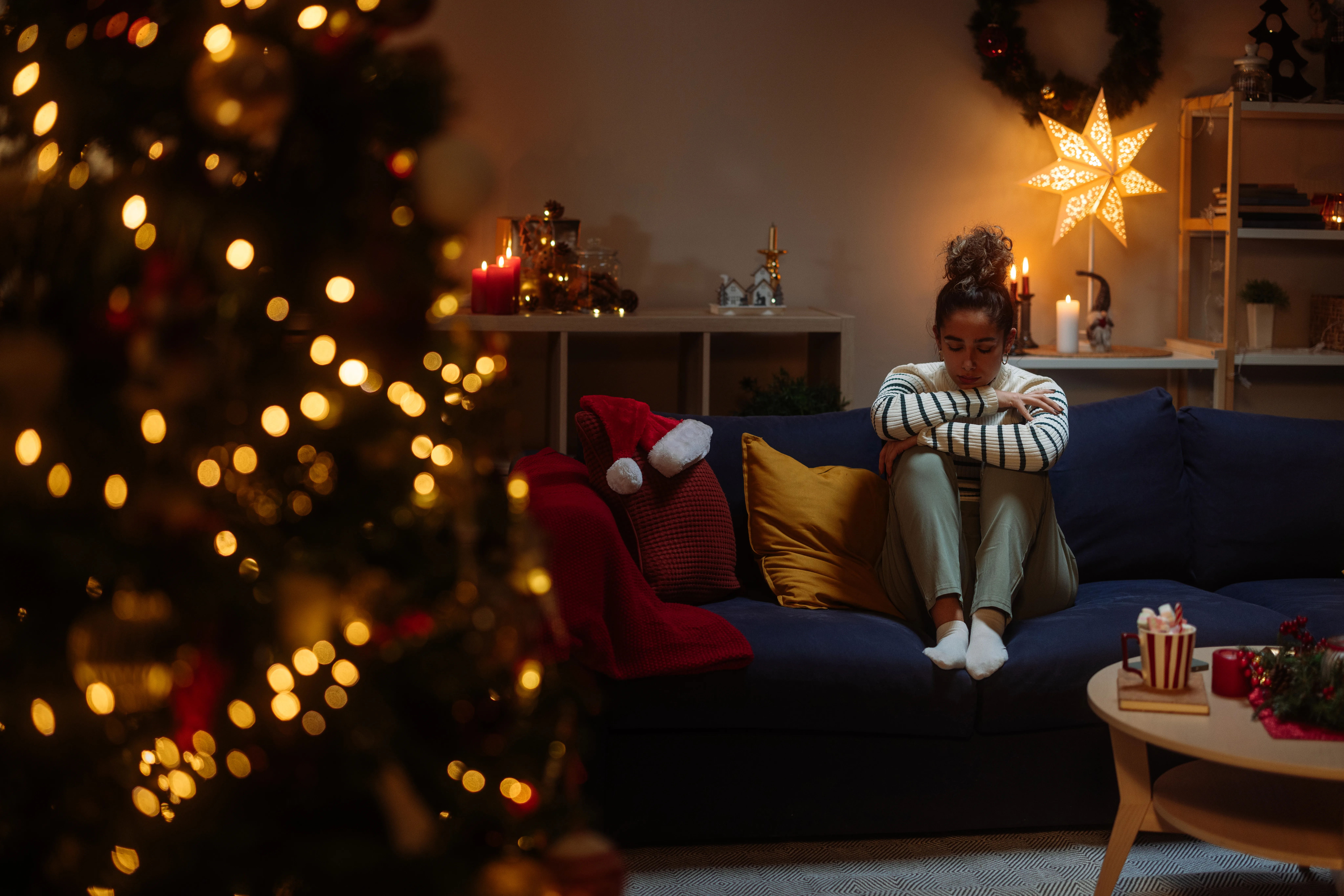 Young woman feeling lonely and depressed during christmas time, sitting on the sofa in a decorated living room