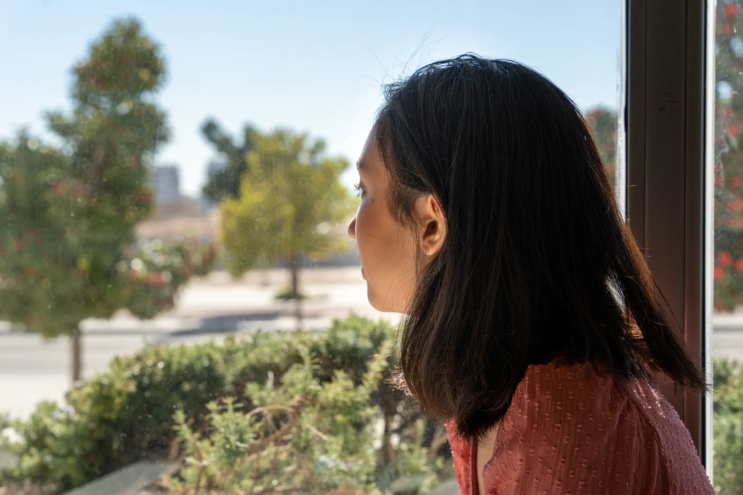 young woman looking out of the window, seeing a park and the sunny day, horizontal close up